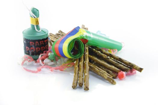 Salty brown tasty pretzels and party blower with party popper and streamers on a reflective white background