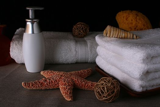 Subjects of personal hygiene: towels, liquid soap and a bast on a dense fabric with decorative elements: a starfish and an aromatic wood.