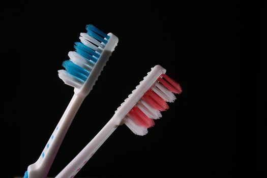 Two tooth-brushes with red and dark blue bristle on black background.