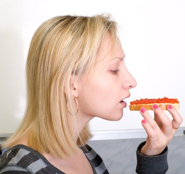 The girl eats a sandwich with red caviar.