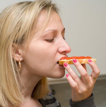 The female bites off a sandwich with red caviar.