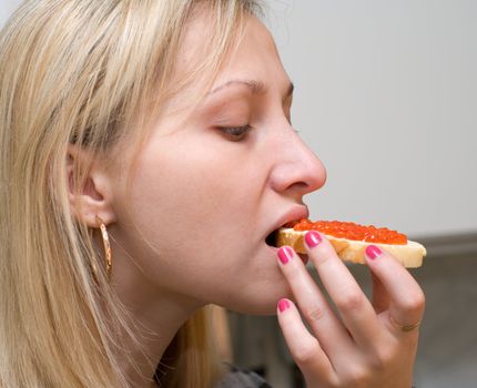 The female bites off a sandwich with red caviar.