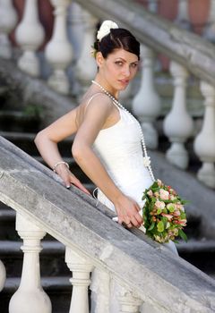 Half body portrait of pretty bride with bouquet of flowers on stone stairs outdoors.