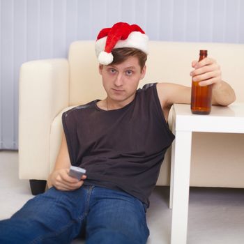 People in christmas hat sits on a floor with beer at the TV