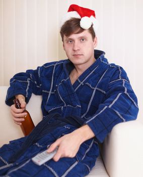 Person in christmas hat sits on a sofa with beer at the TV