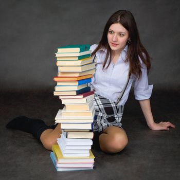 The beautiful schoolgirl with amazement looks at a huge pile of textbooks