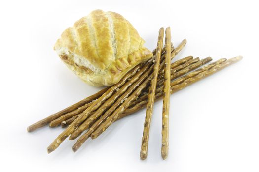 Small tasty sausage roll with salty pretzel  sticks on a reflective white background