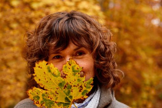 Mature woman hiding behind a  maple leaf in autumn