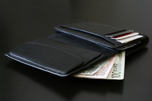 Euro bills coming out of a black wallet.