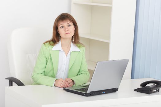 The businesswoman sits at a table at light office with the laptop