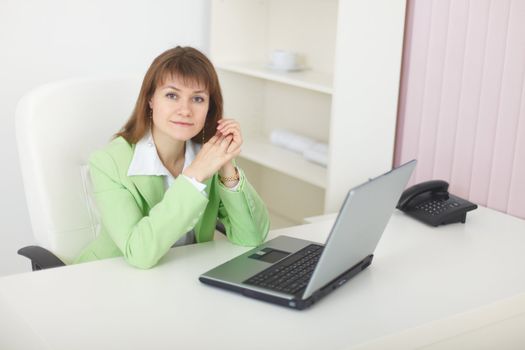 The beauty with the laptop sits at a table at light office