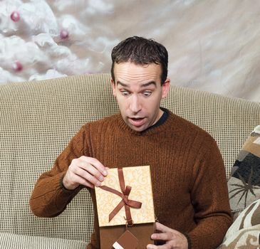 A young man looks surprised at what he sees for his Christmas present