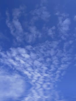 Cloud panorama reflected in calm ocean waters, against summery blue sky