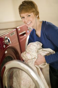 Smiling woman with earphones taking laundry out of dryer 