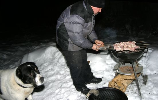 The man makes a shish kebab. The dog waits a meal
