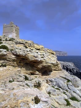 Defense tower on typical rocky coastline in Malta, punctuated with sheer drops and jagged cliffs