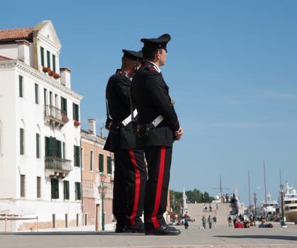 Two Italian police, carabinieri, stand uniformed watching the Venice tourists on Ponte della Paglia, Riva degli Schiavoni, Venice's waterfront promenade, May 2011.