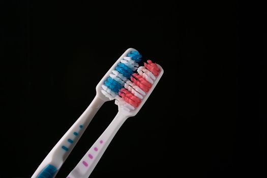 Two tooth-brushes with red and dark blue bristle on black background.