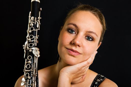 Young beautiful clarinetist woman on black background