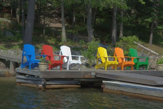 Six Chairs of different colours are resting on the deck and taking in the sunshine