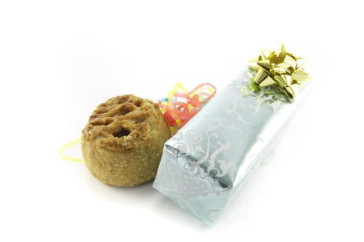 Small pork pie with a silver shiny gift and streamers on a reflective white background