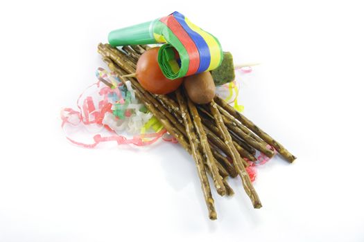 Salty brown tasty pretzels and party blower with cocktail stick containing hot dog, gherkin and tomato with streamers on a reflective white background