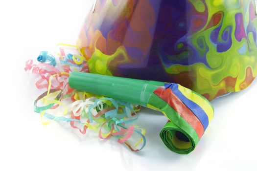 Bright cone shaped party hat and blower with party streamers on a reflective white background
