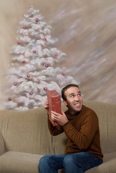 A young man smiling and shaking his Christmas gift to guess what it is, shot in front of a hand painted background