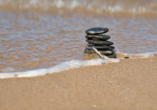 a small tower of stones on the beach about to fall from the wave