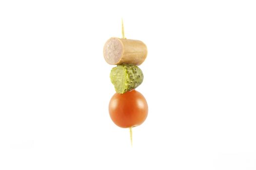 Single cocktail stick with sausage, gherkin and small red tomato on a reflective white background