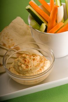 middle eastern hummus dip on a glass bowl with homemade pita brad and raw vegetable