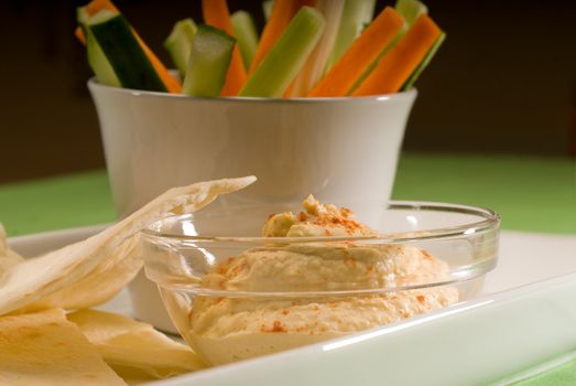 middle eastern hummus dip on a glass bowl with homemade pita brad and raw vegetable