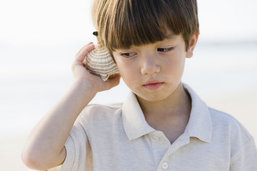 Portrait of a Little Boy Standing at The Beach Listening To A Shell