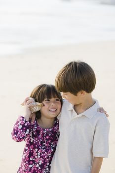 Portrait of Brother and Sister Listening To Shell at Beach