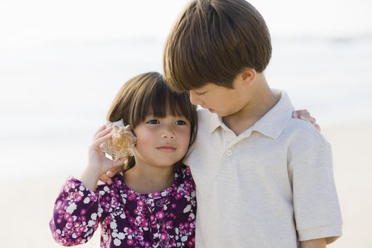 Portrait of Brother and Sister Listening To Shell at Beach