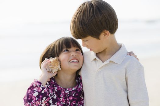 Portrait of Brother and Sister Listening To Shell at Beach