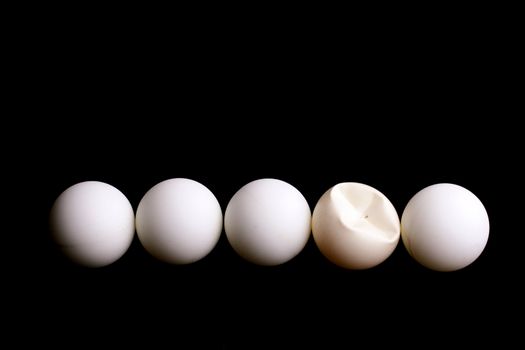 Five balls for game in table tennis on a black background. One ball is rumpled in game.