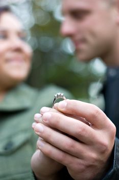 A young happy couple holding a diamond engagement ring.  Shallow depth of field with focus on the ring.