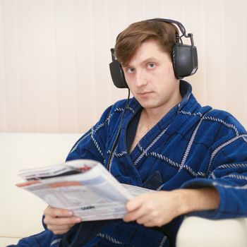 Person in the big ear-phones sits on a sofa reads the newspaper