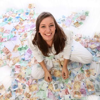 Young woman is sitting happily in the money. She sits on many euro banknotes