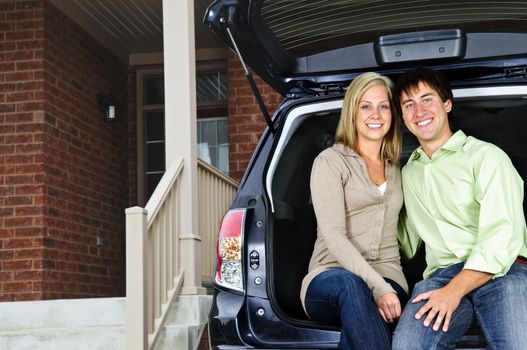 Happy young couple sitting at back of car on driveway