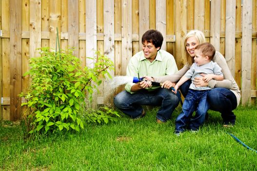 Happy family in backyard watering plant with hose