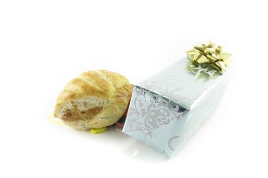 Small tasty sausage roll with silver shiny gift with gold bow and streamers on a reflective white background