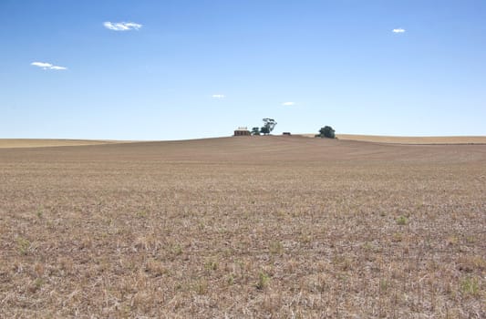 a farm house at the top of a dry field in the drought