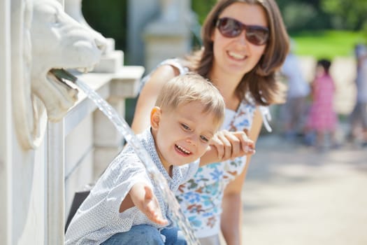 Beautiful Mother with her son playing with water in fountain