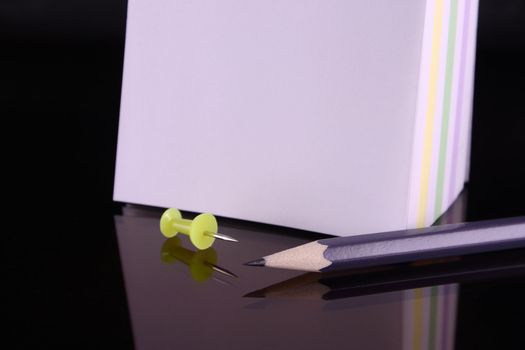 The block for records, a pencil and a pin on dark glass removed close up