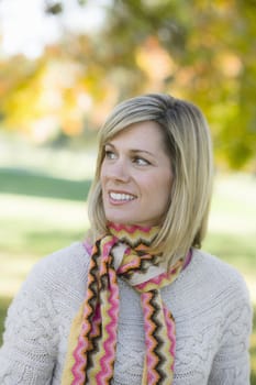 Portrait of a Pretty Blond Woman in a Scarf and Sweater Standing in a Park