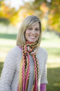 Portrait of a Pretty Blond Woman in a Scarf and Sweater Standing in a Park