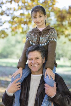 Portrait of a Father Holding Daughter on His Shoulders in a Park