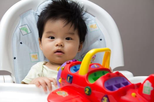 Little Asian baby girl on high chair playing with airplane toy